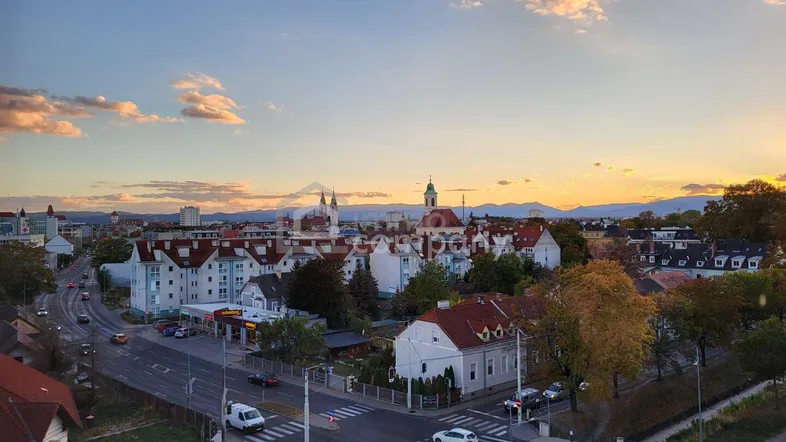 Panoramablick über eine Stadt bei Sonnenuntergang mit Bergen im Hintergrund und belebten Straßen.