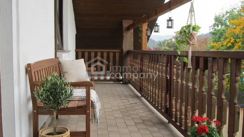 Überdachter Balkon mit Fliesenboden, Holzbank und Blick ins Grüne, ideal zum Entspannen.