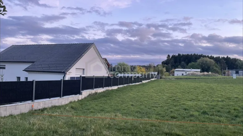 Blick auf ein Grundstück mit einem modernen Haus im Hintergrund und einem schwarzen Zaun.