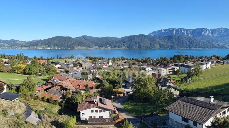 Panoramablick auf eine malerische Stadt am Seeufer mit majestätischen Bergen im Hintergrund.