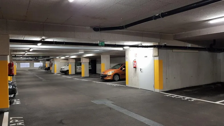 Tiefgarage mit mehreren Stellplätzen, Betonwänden und Decken sowie sichtbaren Installationen.