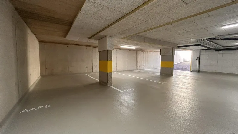 Tiefgarage mit markierten Stellplätzen, Betonwänden und Deckenplatten, gut beleuchtet.