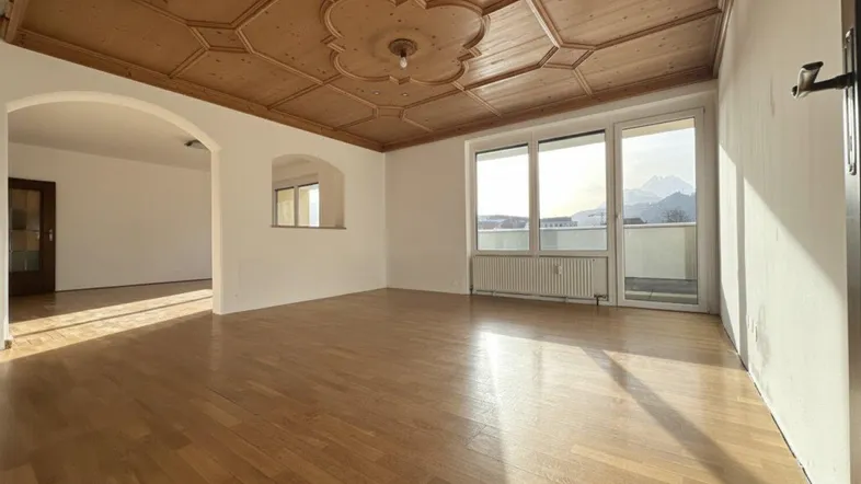 Geräumiges Wohnzimmer mit Holzkassettendecke, Parkettboden und Zugang zum Balkon mit Bergblick.