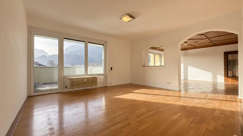 Helles Wohnzimmer mit Holzboden, großen Fenstern und beeindruckendem Bergblick, verbunden durch einen eleganten Bogen.