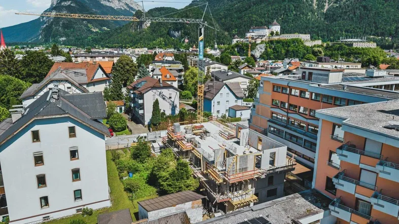 Luftaufnahme einer Baustelle in einer Stadt mit umliegenden Gebäuden und Bergen im Hintergrund.