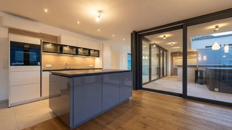 Moderne Küche mit Kücheninsel, integrierten Geräten und Zugang zu einer verglasten Terrasse.