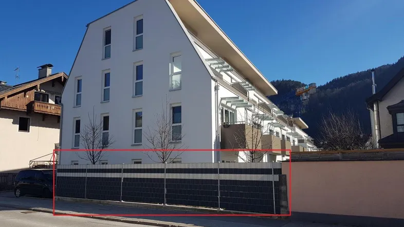 Moderne Wohnanlage mit weißer Fassade, Balkonen und Blick auf die umliegenden Berge.