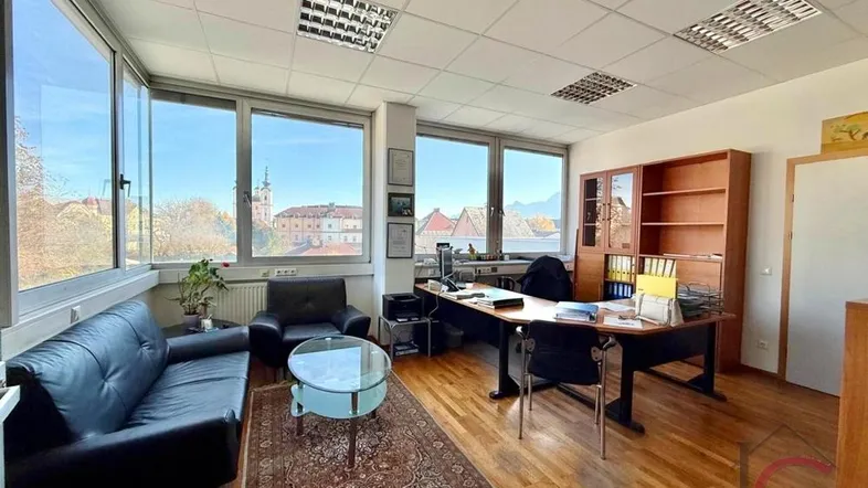 Helles Büro mit großen Fenstern, Holzboden und Blick auf eine Kirche und umliegende Gebäude.