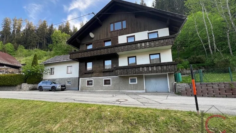 Traditionelles Chalet mit Holzbalkonen und Satteldach, eingebettet in eine grüne Berglandschaft.