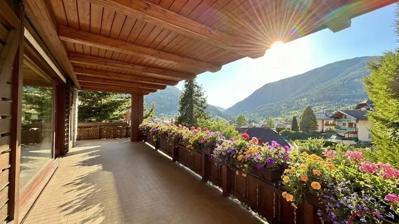 Sonniger Balkon mit Holzboden, Blumenkästen und weitem Blick auf die umliegenden Berge und das Tal.