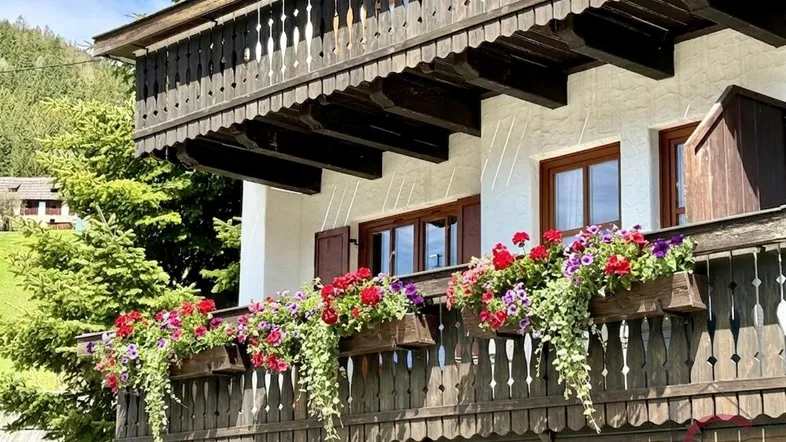 Traditioneller Holzbalkon mit reichlich Blumenkästen und Blick auf die umliegende Natur.
