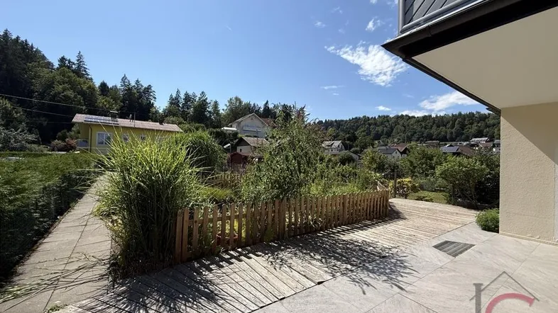 Große Terrasse mit Holzdeck und Fliesenbereich, umgeben von einem kleinen Garten mit Blick ins Grüne.