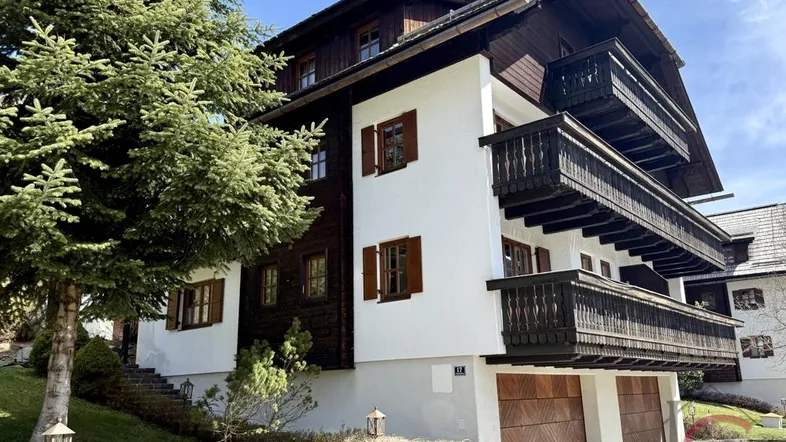 Traditionelles Holzhaus mit weißer Fassade, mehreren Balkonen und integrierter Garage in alpiner Umgebung.