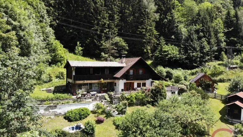 Haus in Hanglage umgeben von Wald und Grünflächen mit Terrassenbereichen und Bergblick.