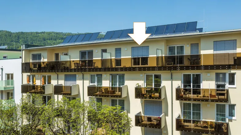 Modernes Mehrfamilienhaus mit Balkonen und Solaranlage auf dem Dach unter blauem Himmel.
