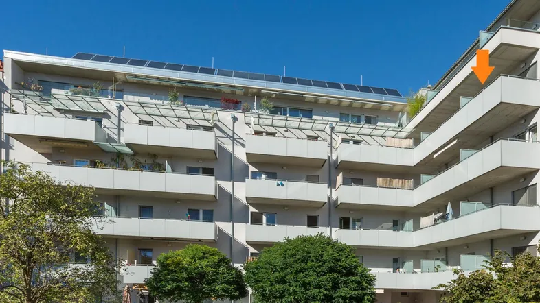 Moderne Wohnanlage mit mehreren Balkonen, Solarpaneelen auf dem Dach und grüner Umgebung.