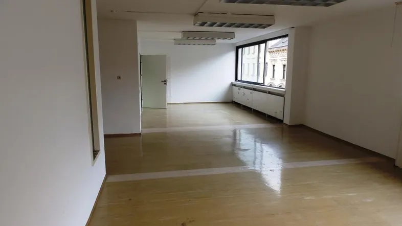Geräumiger, leerer Büroraum mit großen Fenstern, die viel Tageslicht hereinlassen und einen Blick auf die Stadt bieten.