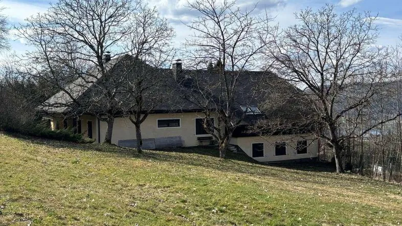 Ländliches Haus mit Satteldach und umgebender Natur auf einem grünen Hügel.