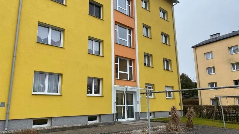Gelbes Mehrfamilienhaus mit orangefarbenen Akzenten und gepflegtem Vorgartenbereich.