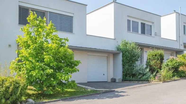 Reihenhäuser mit moderner Architektur, weißen Fassaden, Garagen und grüner Umgebung.