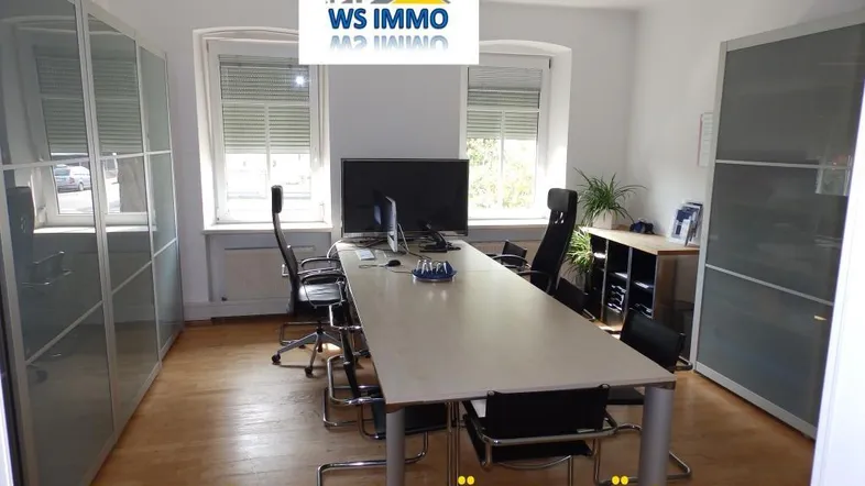 Helles Büro mit modernem Konferenztisch, Bürostühlen und großen Fenstern mit Jalousien.
