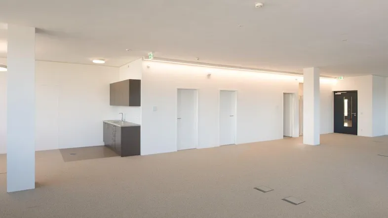 Geräumiger, heller Büroraum mit Teppichboden, integrierter Küchenzeile und Säulenstruktur.