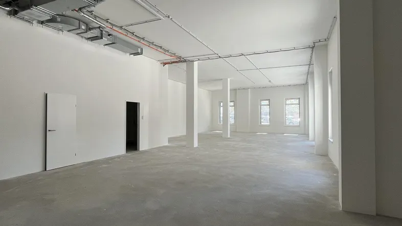 Großer, leerer Gewerberaum mit hohen Decken, sichtbaren Installationen und vielen Fenstern.