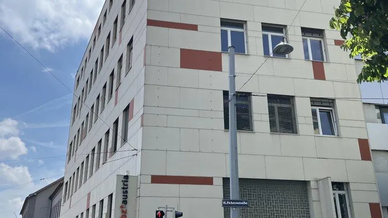 Modernes Bürogebäude mit hellen Fassadenplatten und roten Akzenten an einer städtischen Straße.