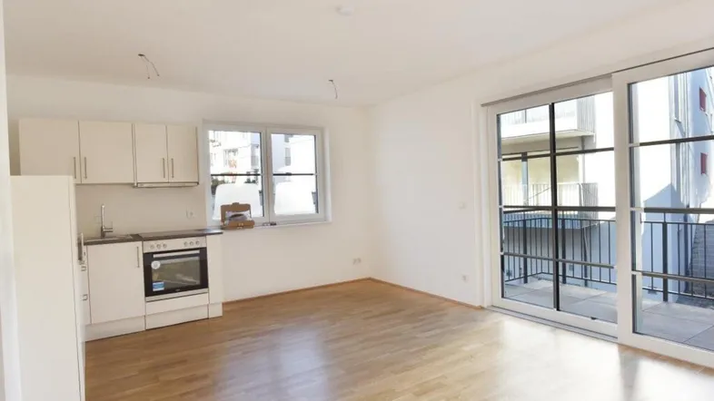 Heller offener Wohnbereich mit integrierter Küchenzeile und Zugang zu einem Balkon.