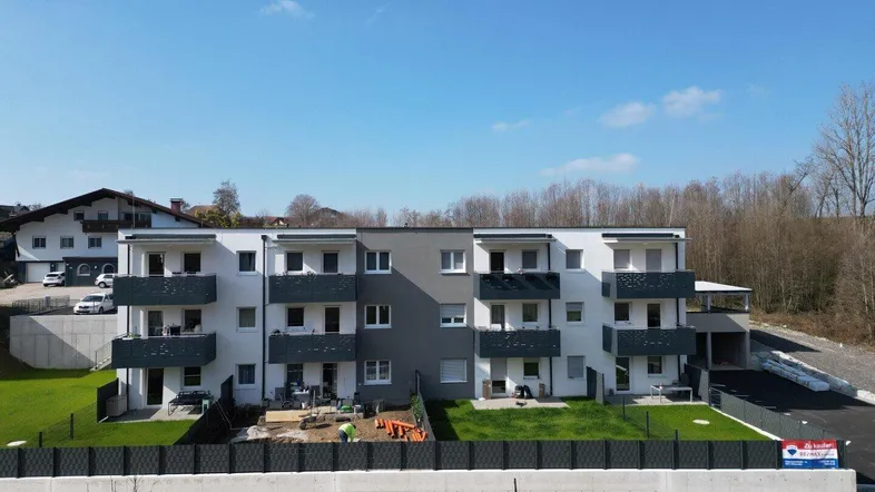 Modernes Mehrfamilienhaus mit mehreren Balkonen und gepflegten Grünflächen im Außenbereich.