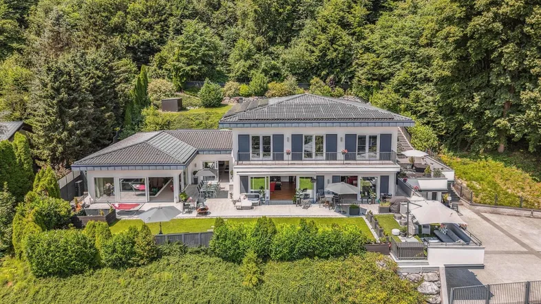 Luftaufnahme des modernen Hauses mit weitläufigen Terrassen und umgeben von grüner Natur.