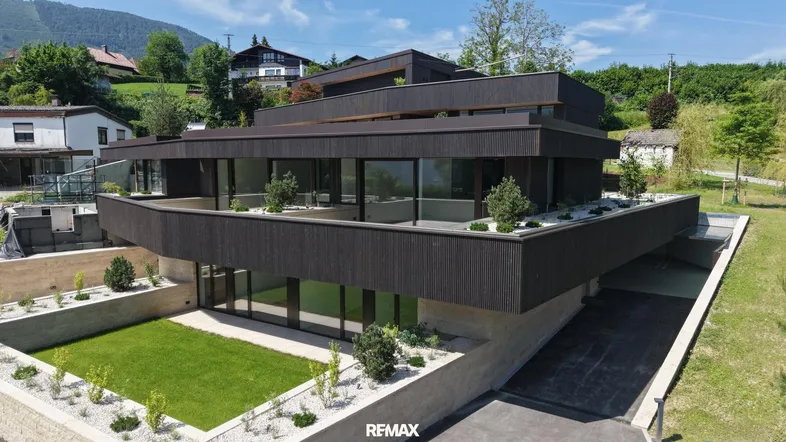 Moderne Architektur mit dunkler Fassade, großen Fenstern und begrünten Terrassenbereichen.