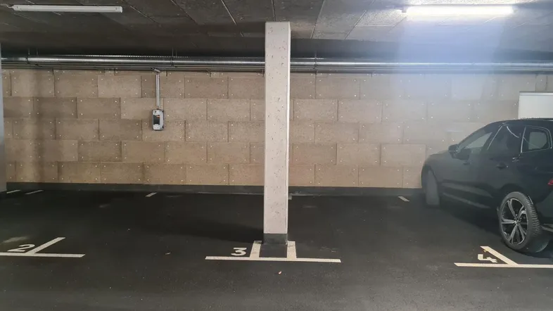 Tiefgarage mit markierten Stellplätzen, einer Ladesäule für Elektrofahrzeuge und funktionaler Beleuchtung.