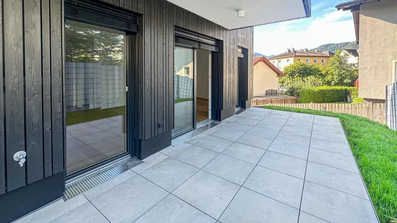 Große geflieste Terrasse mit Zugang zum modernen Neubau und Blick ins Grüne.