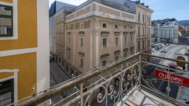 Blick von einem Balkon mit schmiedeeisernem Geländer auf umliegende historische Gebäude und eine belebte Straße.