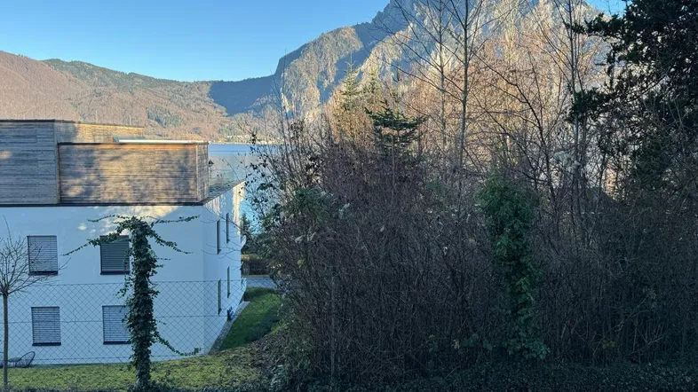 Blick auf ein modernes Gebäude mit See- und Bergblick in sonniger Umgebung.