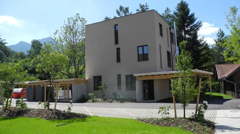 Modernes Gebäude mit schlichter Fassade, umgeben von Grünflächen und mit Carport-Stellplätzen.