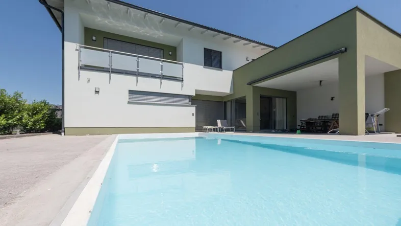 Modernes Haus mit Swimmingpool und überdachtem Essbereich im Freien, umgeben von grüner Landschaft.