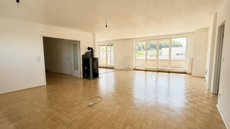 Geräumiges Wohnzimmer mit Parkettboden, Kaminofen und Zugang zu einem Balkon.