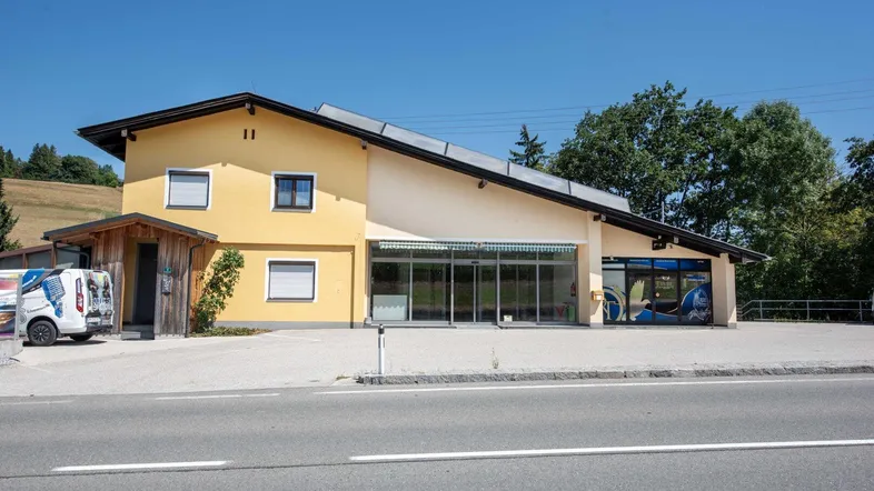 Gebäudeansicht eines Gewerbeobjekts mit gelber Fassade, großen Glasfronten und Solarpaneelen auf dem Dach.