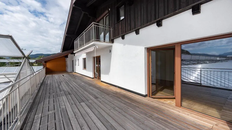 Große Holzterrasse mit Zugang zu den Innenräumen und einem kleinen Balkon darüber.