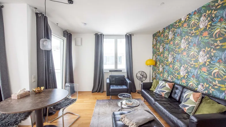 Heller Wohn- und Essbereich mit auffälliger Tapete, Ledersofa und Zugang zum Balkon.