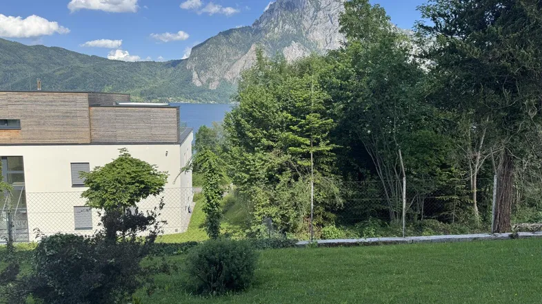 Grüne Rasenfläche mit Blick auf den See und die umliegenden Berge unter blauem Himmel.
