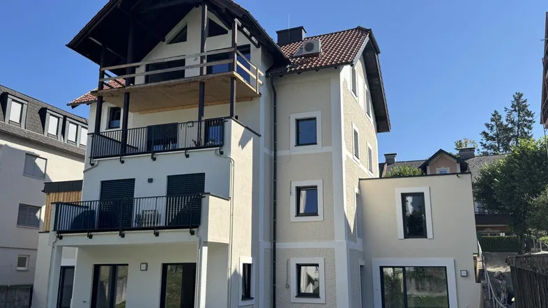 Rückansicht eines Neubaus mit mehreren Balkonen und Terrassen, umgeben von einer Grünfläche.