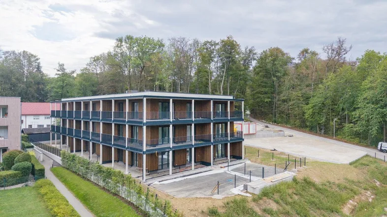 Modernes Mehrfamilienhaus mit Balkonen, umgeben von viel Grün und Waldrandlage.