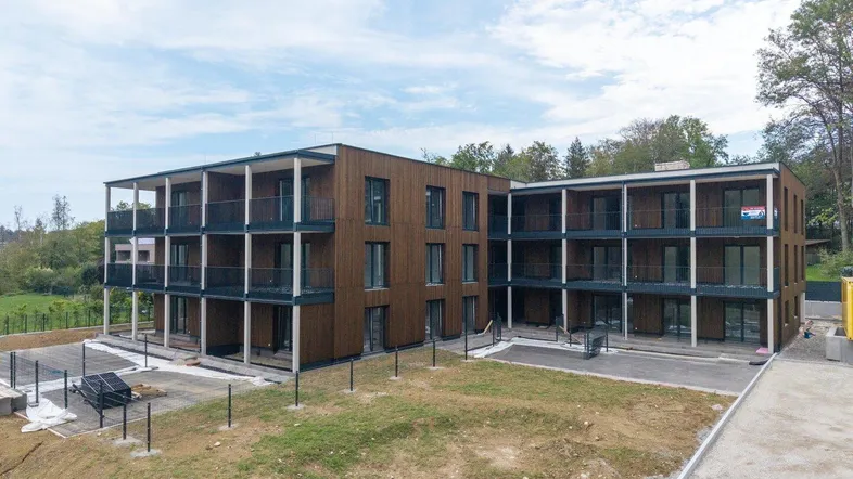 Modernes Mehrfamilienhaus mit Holzfassade, großen Balkonen und Blick ins Grüne, umgeben von Natur.