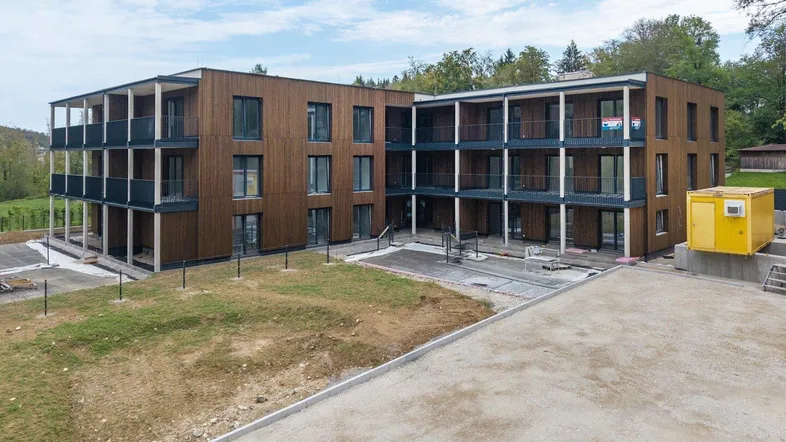 Modernes Mehrfamilienhaus mit Holzfassade und mehreren Balkonen, umgeben von noch unfertigem Gelände.