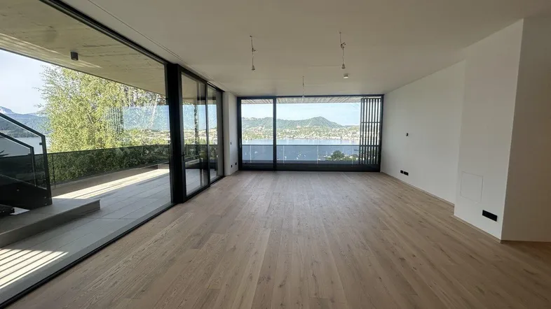 Geräumiges Wohnzimmer mit hellen Holzböden, raumhohen Fenstern und atemberaubendem See- und Bergblick.