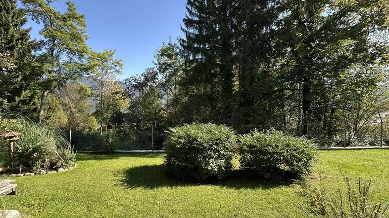 Gepflegter Gartenbereich mit Rasenfläche, Sträuchern und Blick auf die umliegende Natur und Berge.