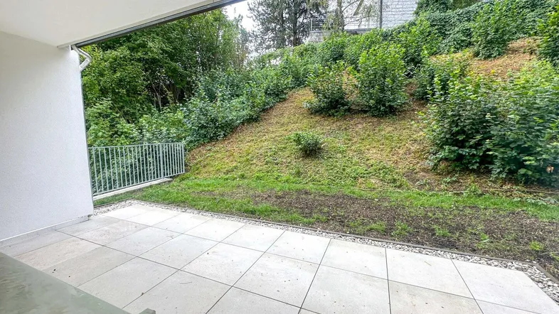 Geflieste Terrasse mit Blick auf eine begrünte Böschung und Bäume, ideal für Entspannung im Freien.
